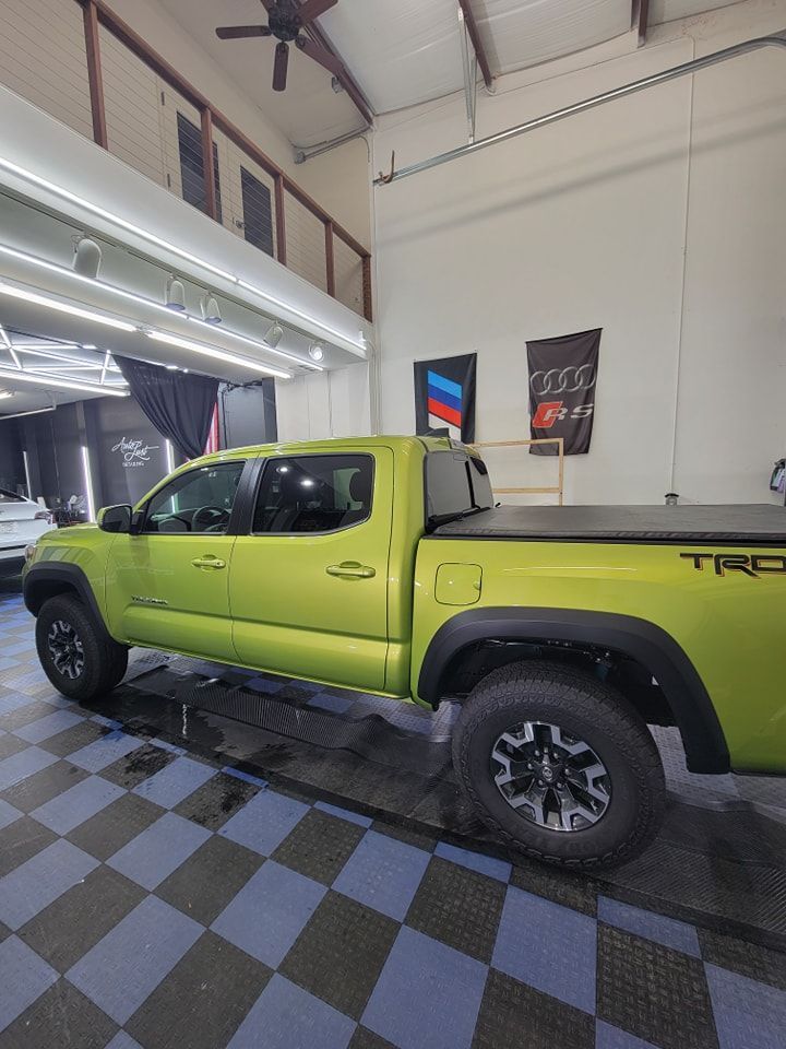 A lime green Toyota Tacoma TRD truck parked on a blue and grey checkered floor in a well-lit garage.