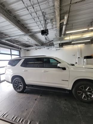 A white Chevrolet Tahoe parked in a garage with high ceilings and industrial lighting.