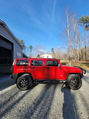 A bright red Hummer parked on a gravel driveway in front of a grey building under a clear blue sky.