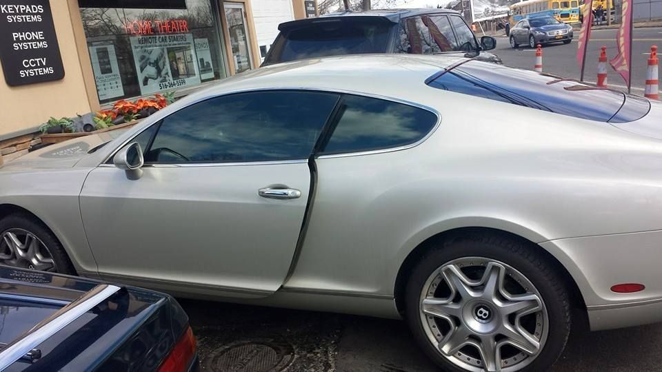 A silver Bentley Continental GT coupe parked on a city street, seen from a side profile view.