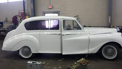 A pristine white classic luxury sedan with whitewall tires parked inside a garage workshop.
