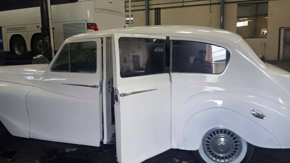 A white vintage car with its rear passenger-side suicide door open, parked inside a garage.