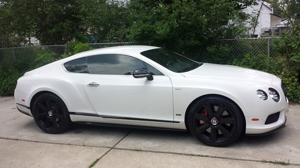 A white Bentley Continental coupe parked on a concrete driveway with black wheels and tinted windows.