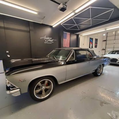 A two-tone black and silver classic convertible car parked inside a garage with a black wall and US flag decor.