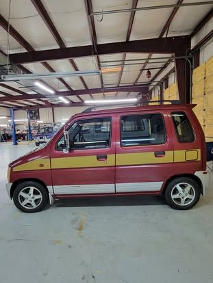 A red and yellow hatchback parked inside a large, industrial-style garage with high ceilings and fluorescent lighting.
