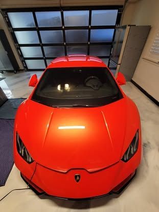 High-angle view of a bright orange Lamborghini parked inside a modern garage with a glass-paned door.