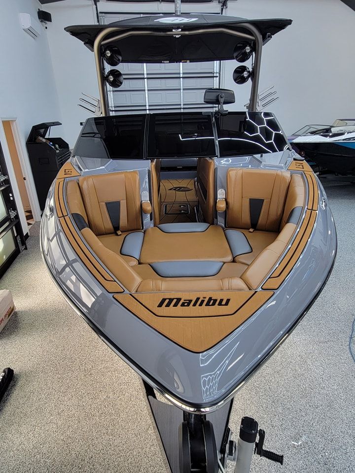 A grey Malibu motorboat with tan interior upholstery parked inside a bright garage.