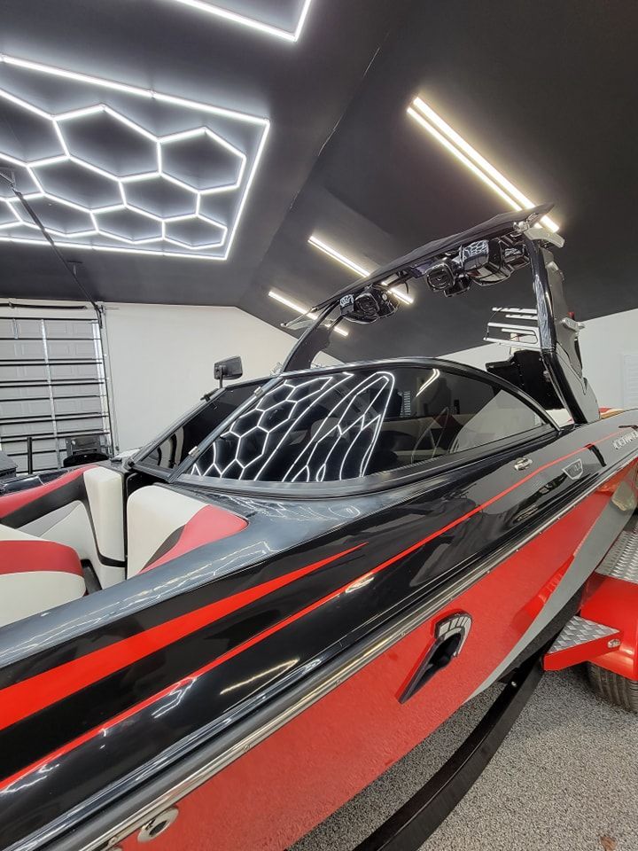 A black and red motorboat parked indoors under decorative geometric ceiling lights, showing a sleek windshield and seating.