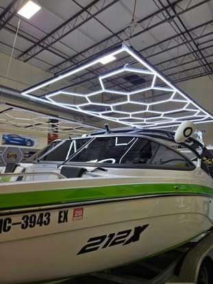 A white and green Yamaha 212X boat parked under modern hexagonal LED ceiling lights in a showroom.