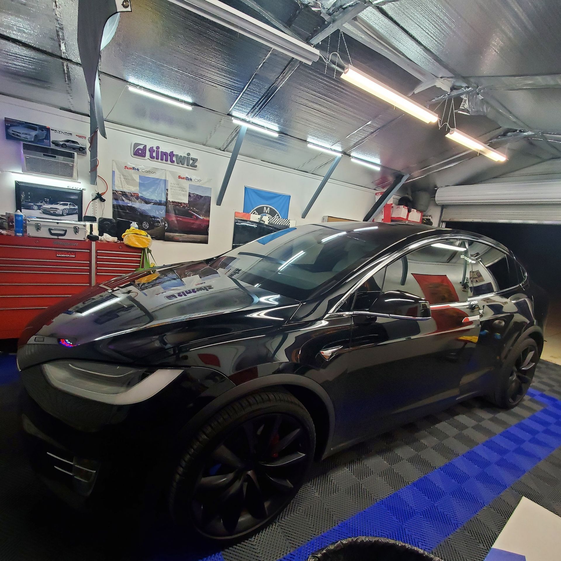 A black Tesla SUV parked inside a well-lit workshop with red storage cabinets and a tiled floor.