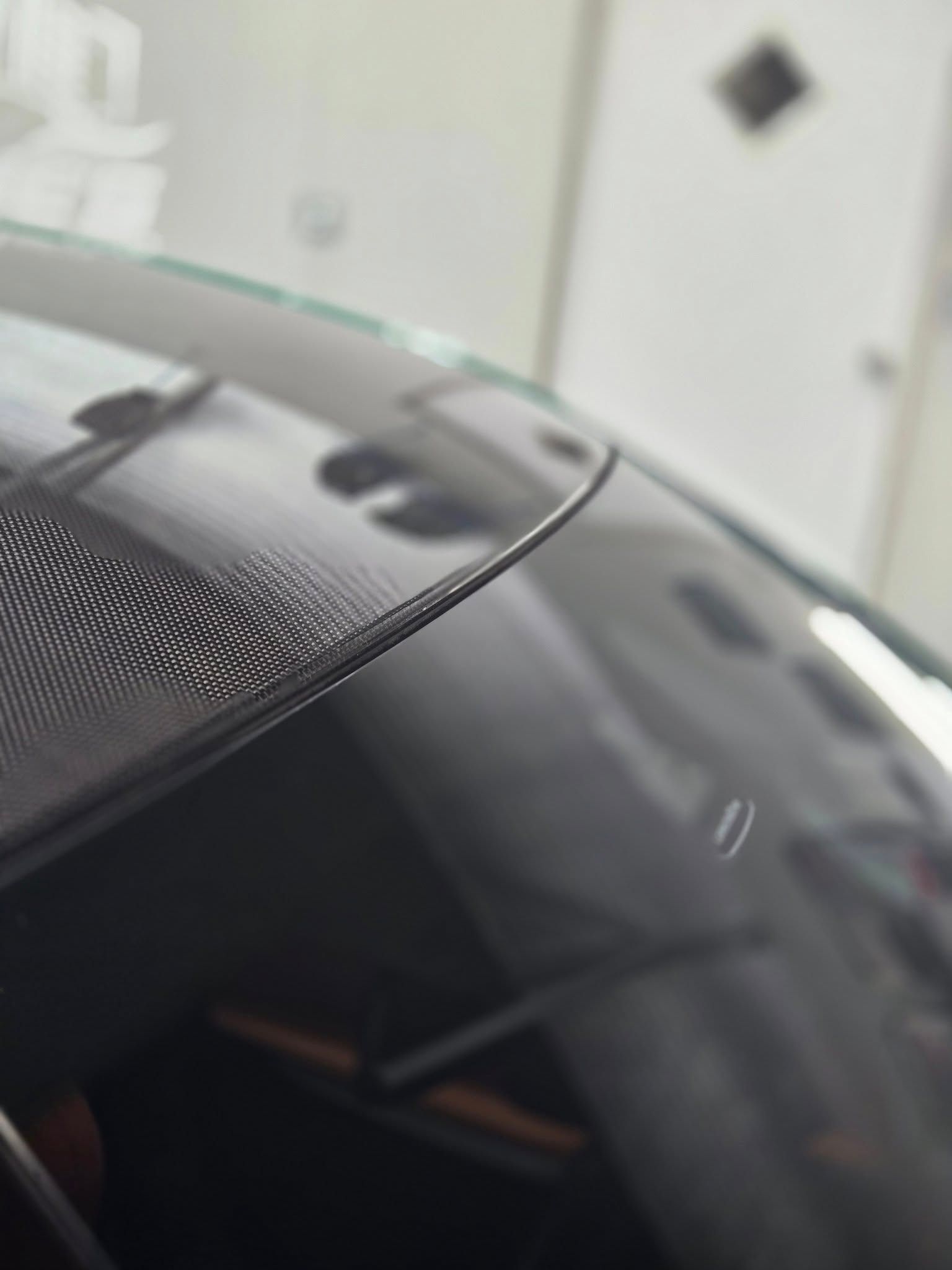 Close-up of a car windshield edge featuring a dotted black frit border, with a blurred interior visible through the glass.