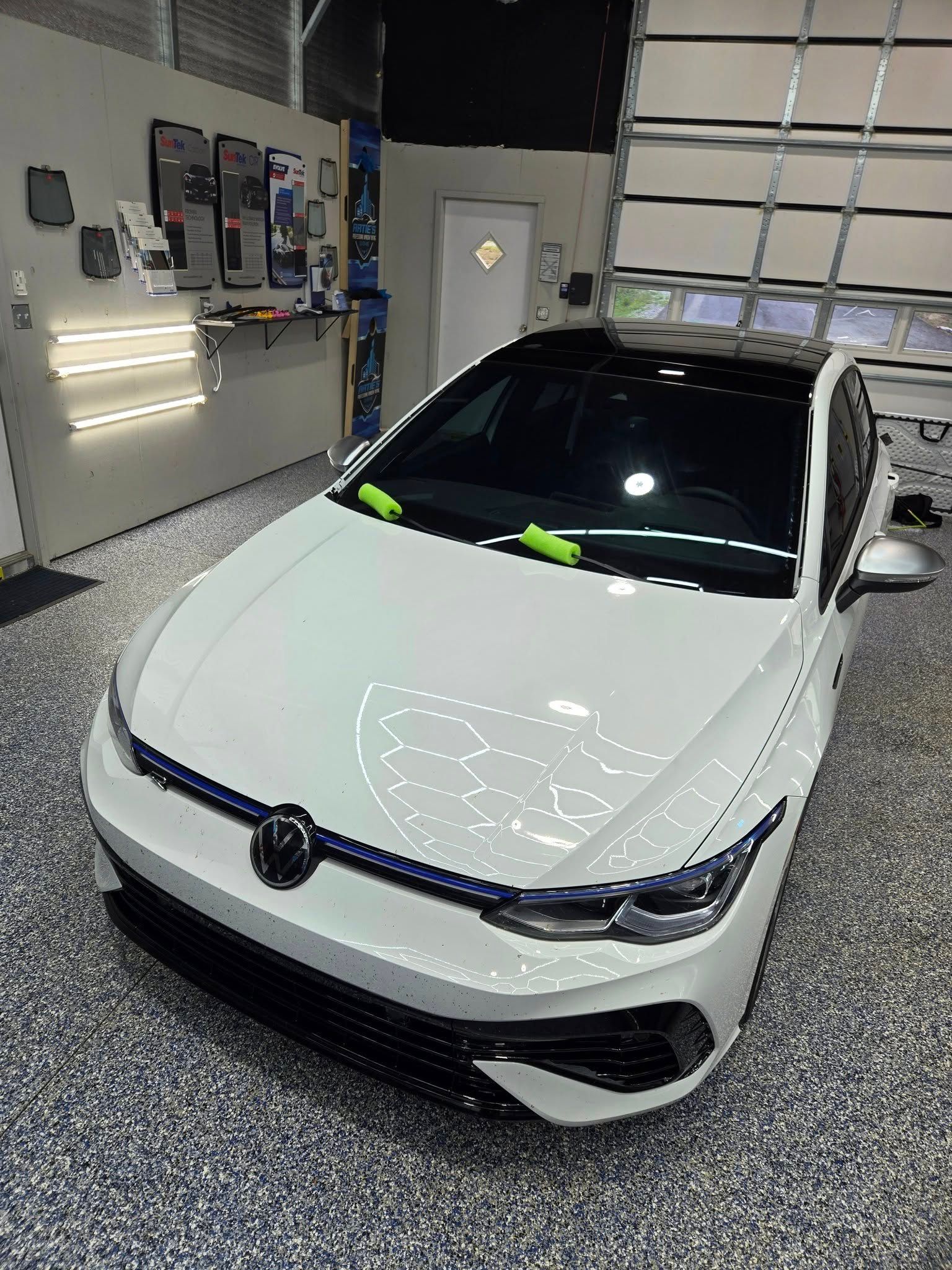 White Volkswagen Golf with a black roof and side mirrors parked in a bright garage with a speckled floor.