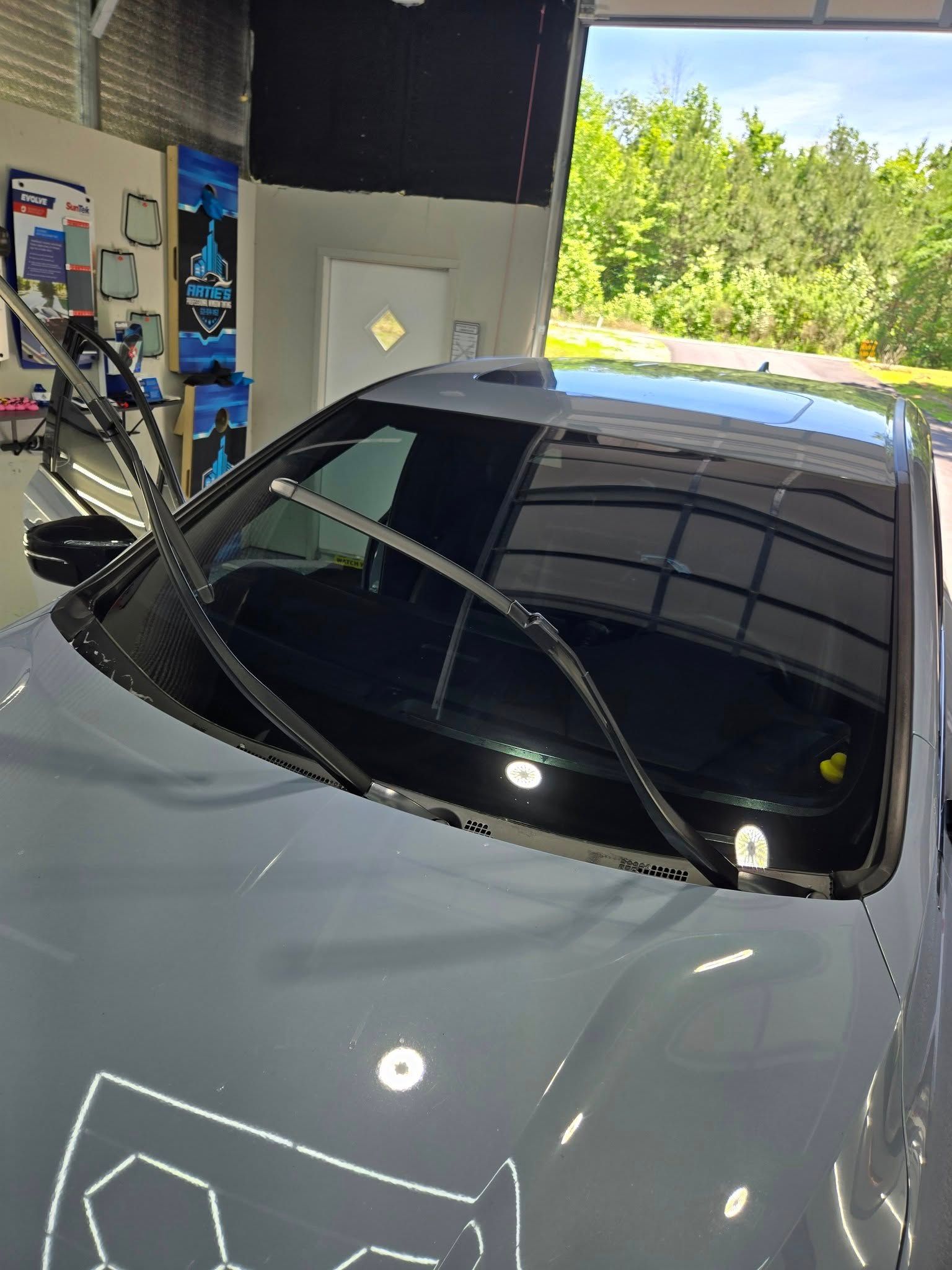 A grey car parked in a garage with windshield wipers lifted away from the windshield.
