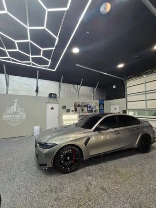 A metallic silver BMW sedan parked inside a modern garage with hexagon-patterned ceiling lights and speckled flooring.