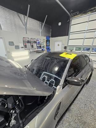 A silver car with a wet windshield and a yellow tool inside a professional garage.