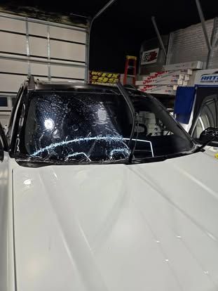 A white vehicle with a severely cracked windshield parked inside a garage.