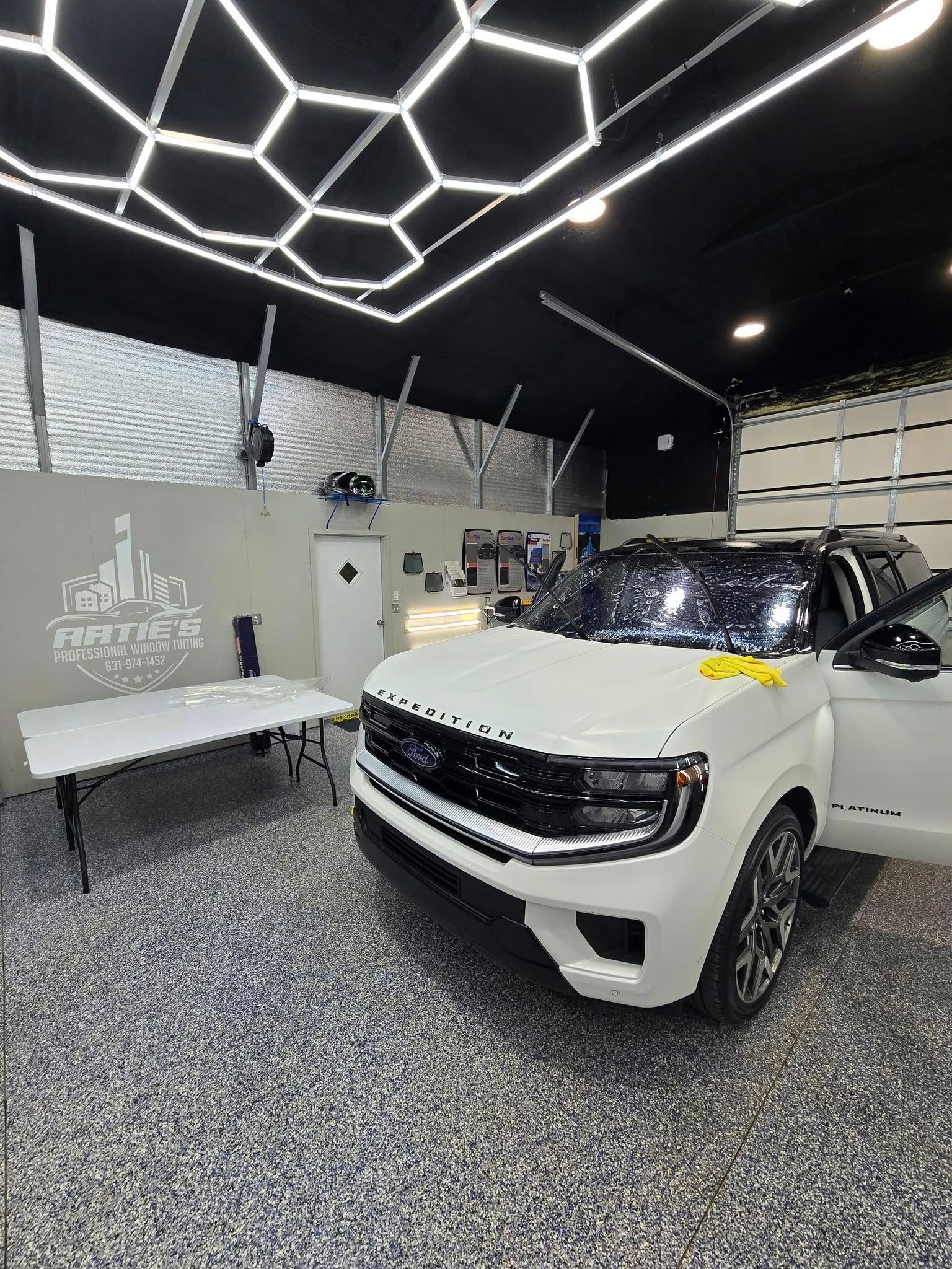 A white SUV parked in a garage with honeycomb LED ceiling lights and a speckled gray floor.