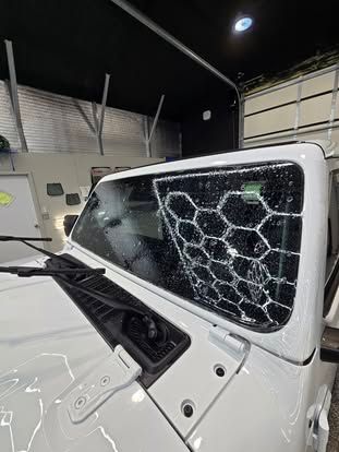 A close-up of a white Jeep windshield showing water beads forming a distinct honeycomb pattern in a garage setting.