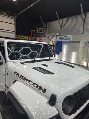 White Jeep Rubicon parked in a garage with a hexagonal-patterned glare reflecting on the windshield.