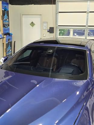 A blue sedan parked inside a garage, with a clear view of its windshield, roof, and hood.