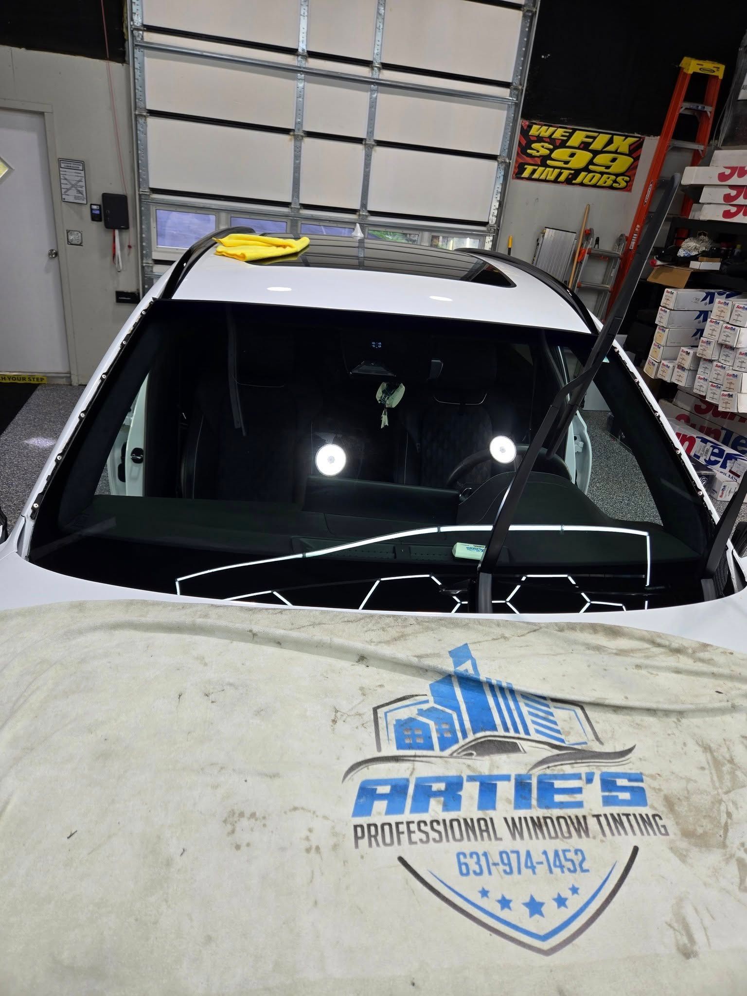 A white car with a protective cloth over the hood inside a garage, highlighting professional window tinting services.