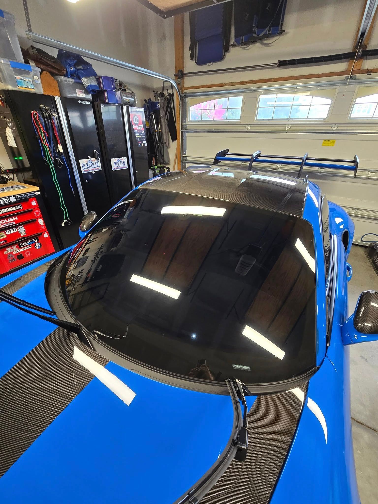 A bright blue sports car with carbon fiber accents is parked inside a garage featuring tall, dark storage cabinets.