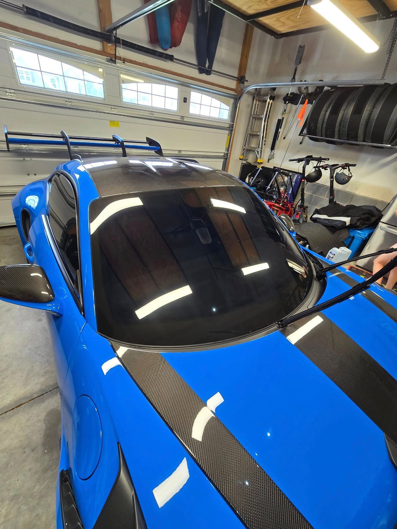A bright blue sports car with a carbon fiber hood and roof parked inside a garage.