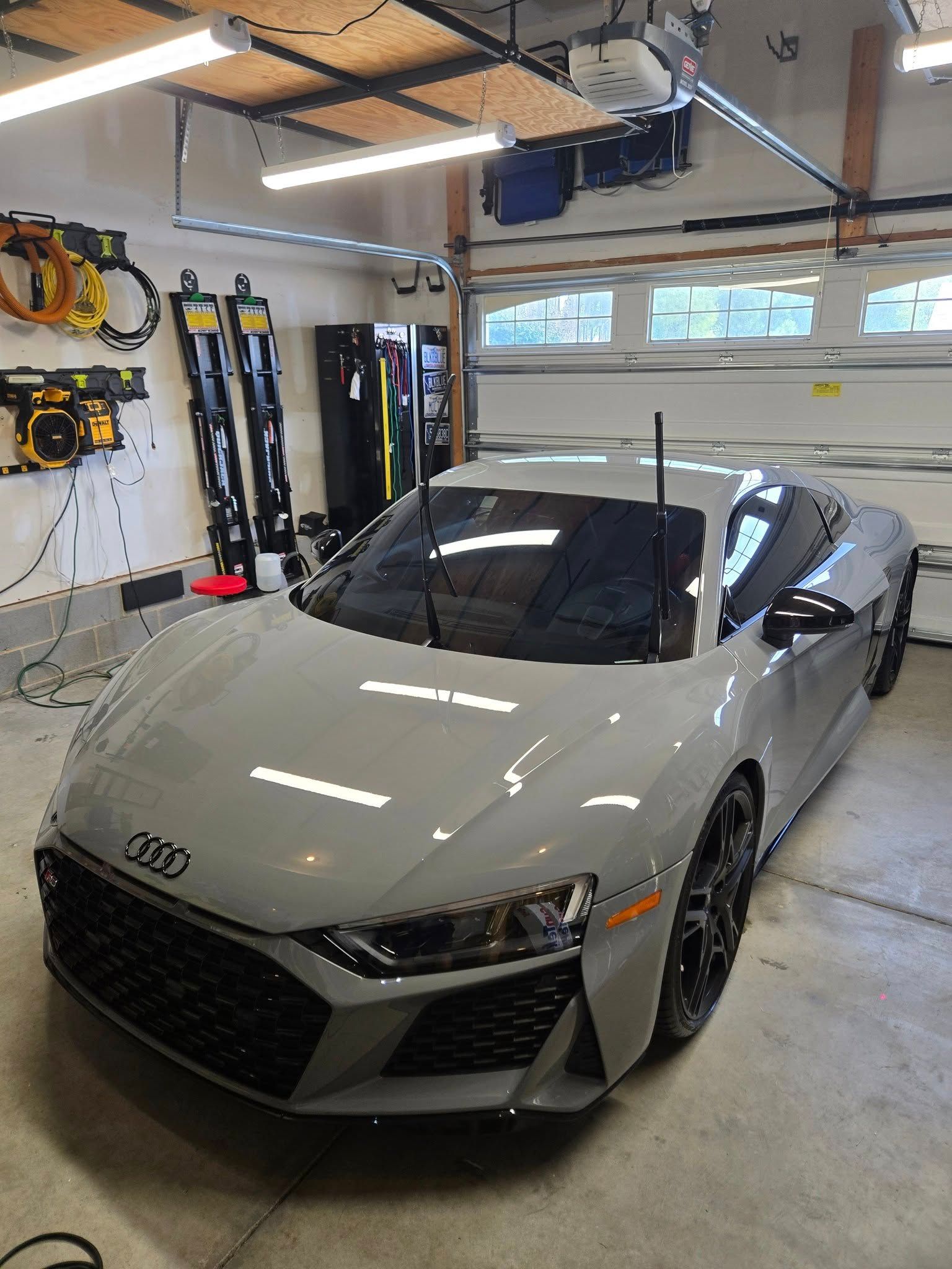 A sleek gray Audi R8 sports car with its windshield wipers raised, parked inside a well-lit residential garage.