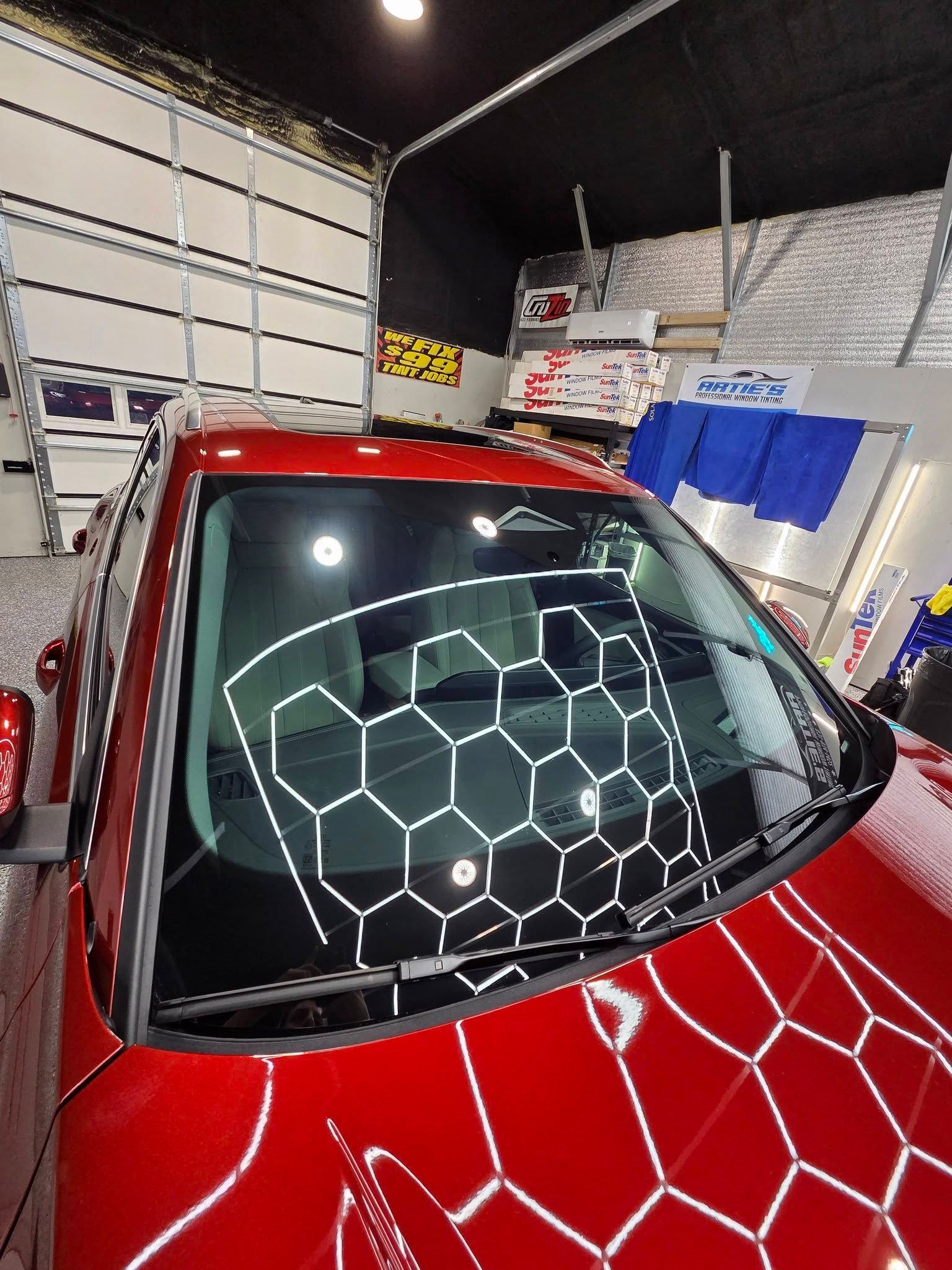 A red car in a garage with a white hexagonal light pattern reflecting on its windshield and hood.