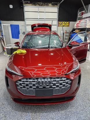 A shiny, red Audi SUV parked in a workshop with its windshield wipers raised and doors open.
