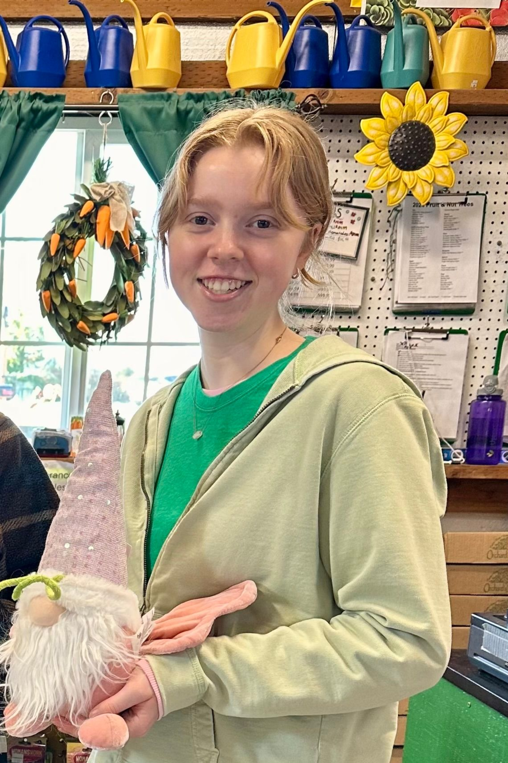 Man in green hoodie and cap, smiling outdoors, hands in pockets.