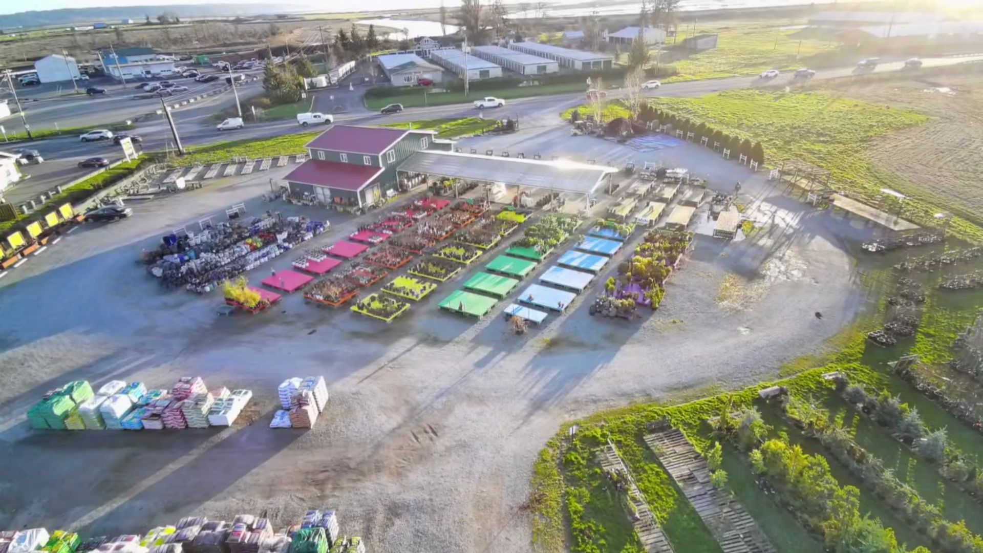 Aerial view of a garden center with rows of colorful plants, a building, and a parking area.
