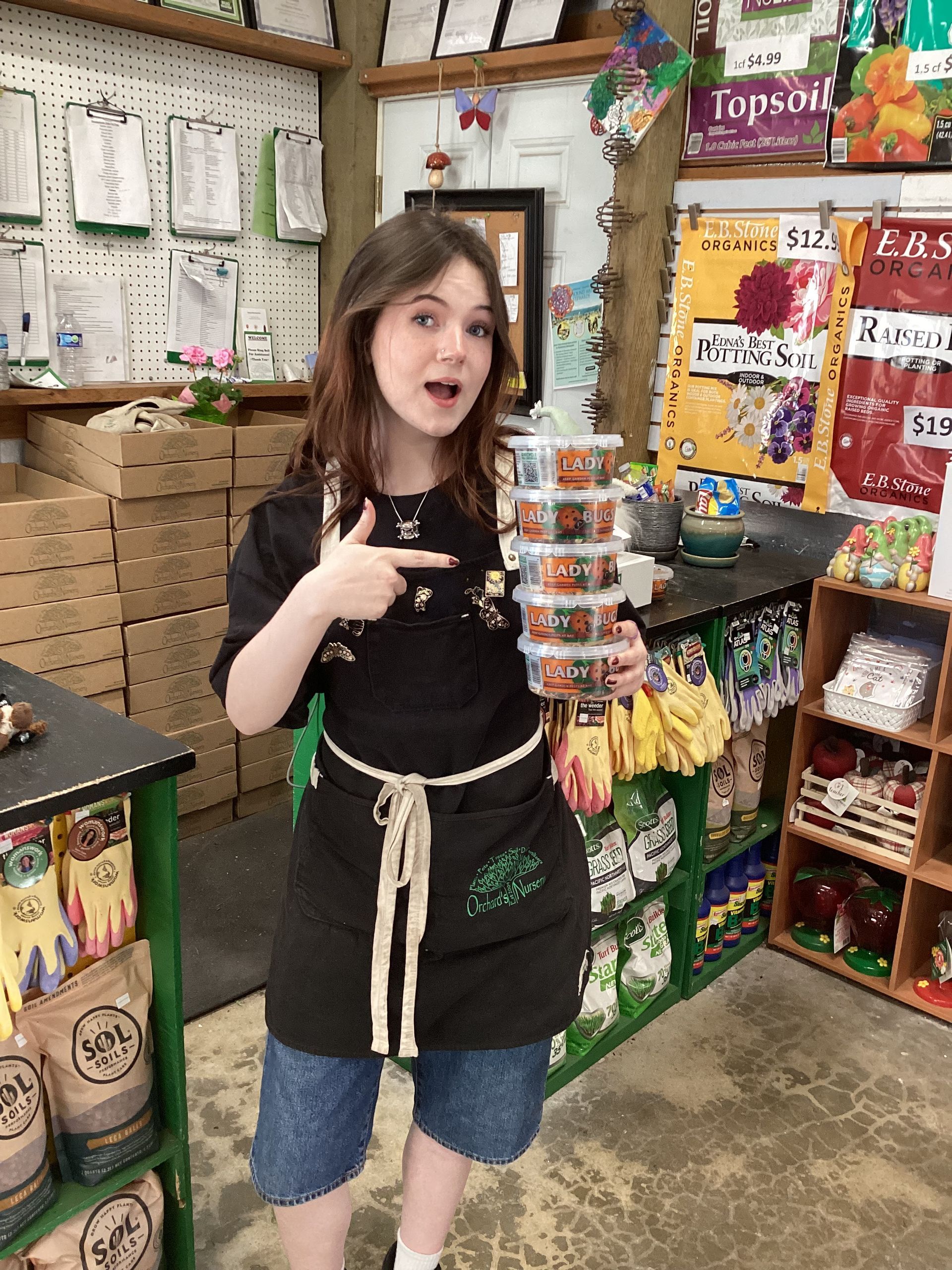 A young person in an apron points to a stack of containers in a store.