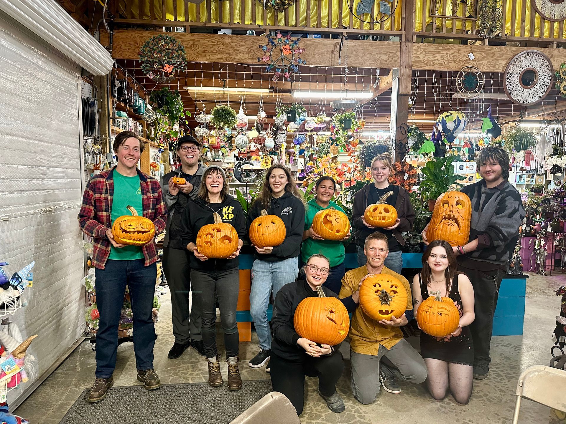 Group of people with carved pumpkins posing inside a decorated shop.