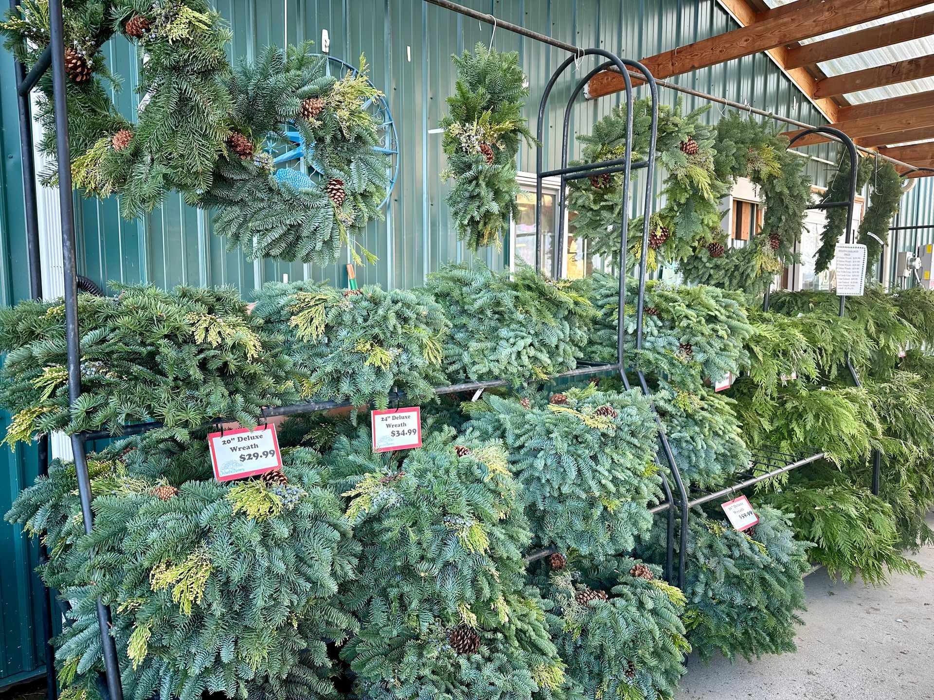 Wreaths for sale at a market, many green fir and pine, some with decorations.