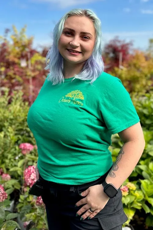 Woman with blue hair in green shirt, smiling outdoors.