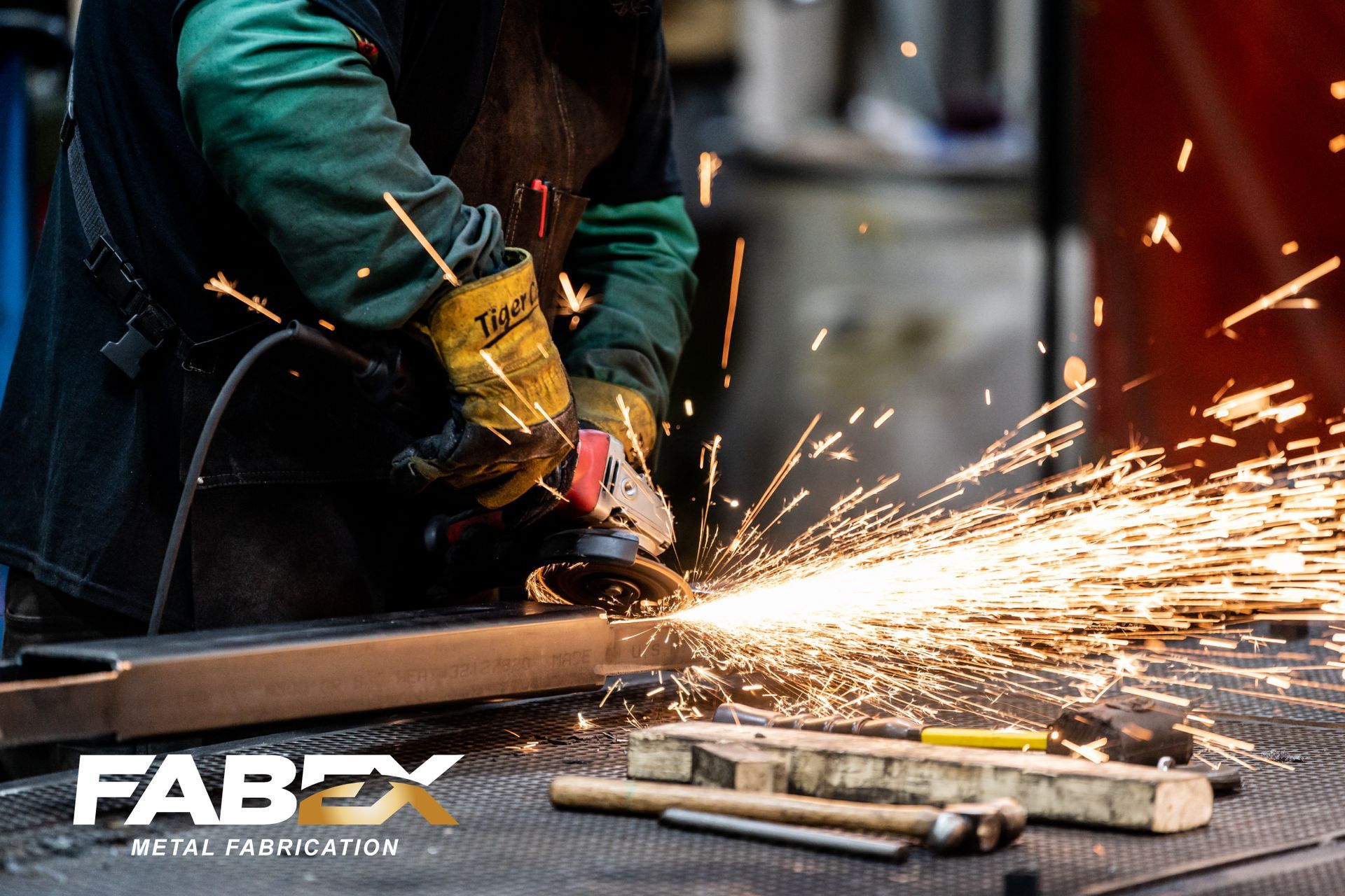 Worker using an angle grinder on metal, sending bright sparks across a workshop floor.