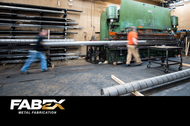 Industrial workshop with workers moving long metal pipes beside a large green machine, FABEX logo visible