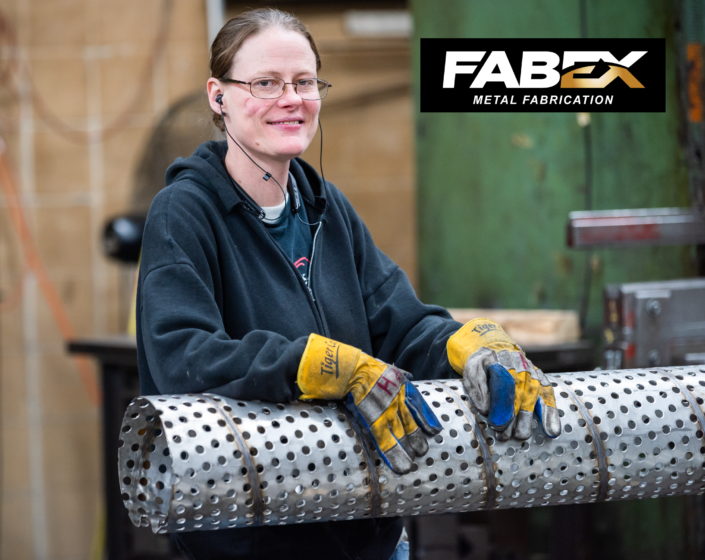 Worker in gloves holding a perforated metal cylinder in a fabrication shop, with FABX logo at top right.
