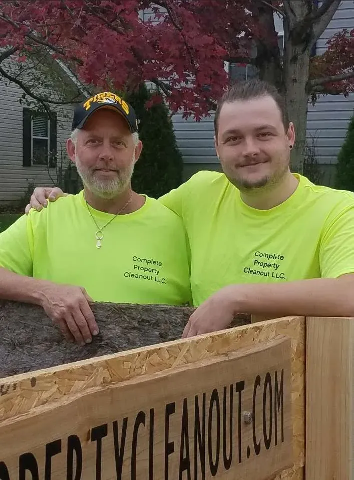 Two men in neon shirts with Property Cleanout logo by a wooden box.