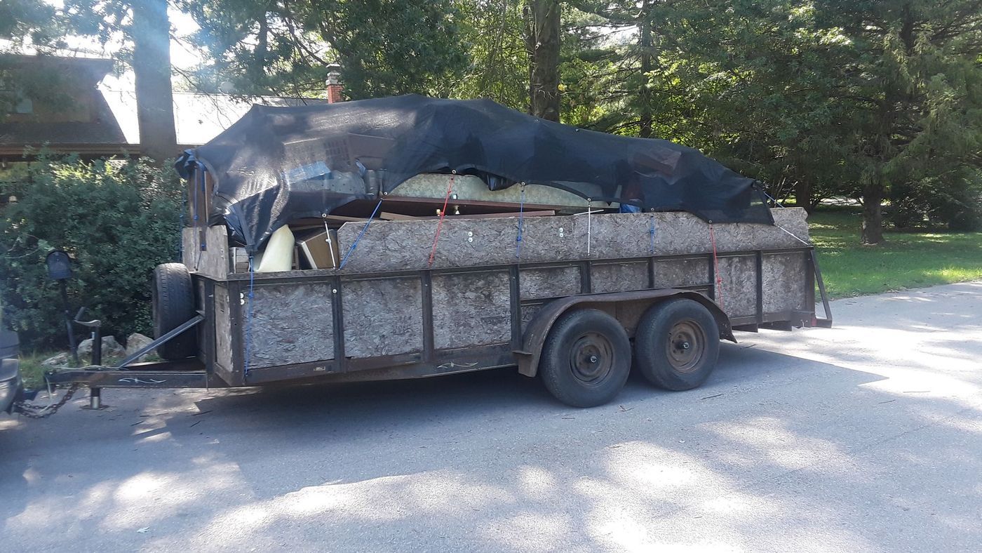A trailer loaded with debris and covered with a black tarp parked on a paved road.