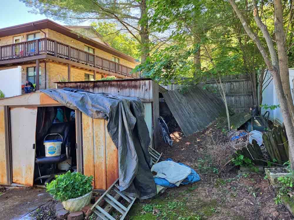 Backyard with damaged shed, debris, and two-story house.