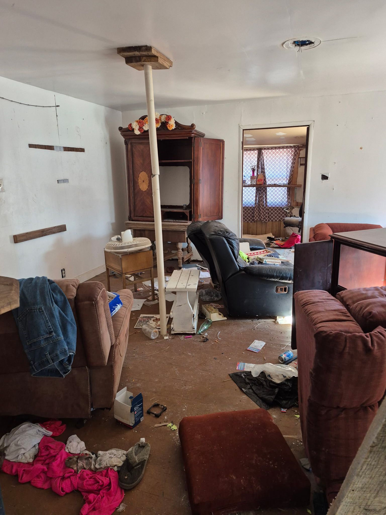 Messy interior of a dilapidated building with debris, exposed wood beams, and trash scattered throughout.