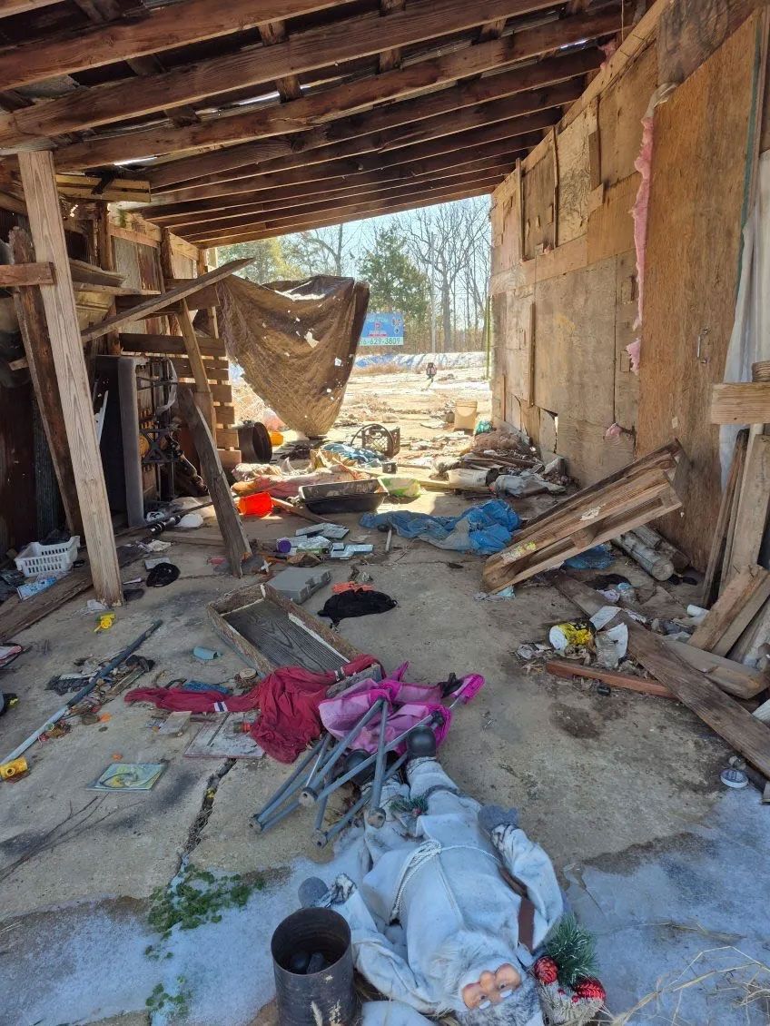Messy interior of a dilapidated building with debris, exposed wood beams, and trash scattered throughout.