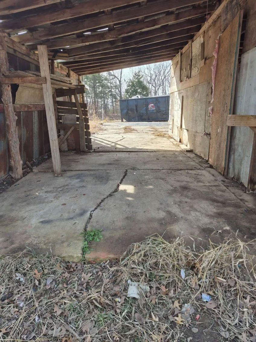 Dilapidated shed interior, concrete floor, open front, view of target practice area, dry foliage.