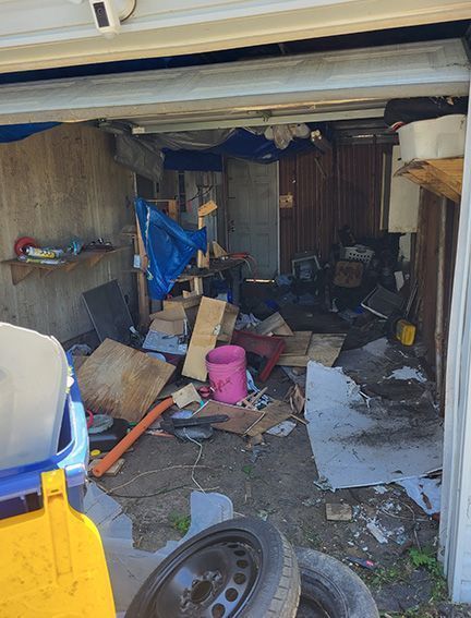 Garbage and debris pile near a tree in a snowy field on a sunny day.