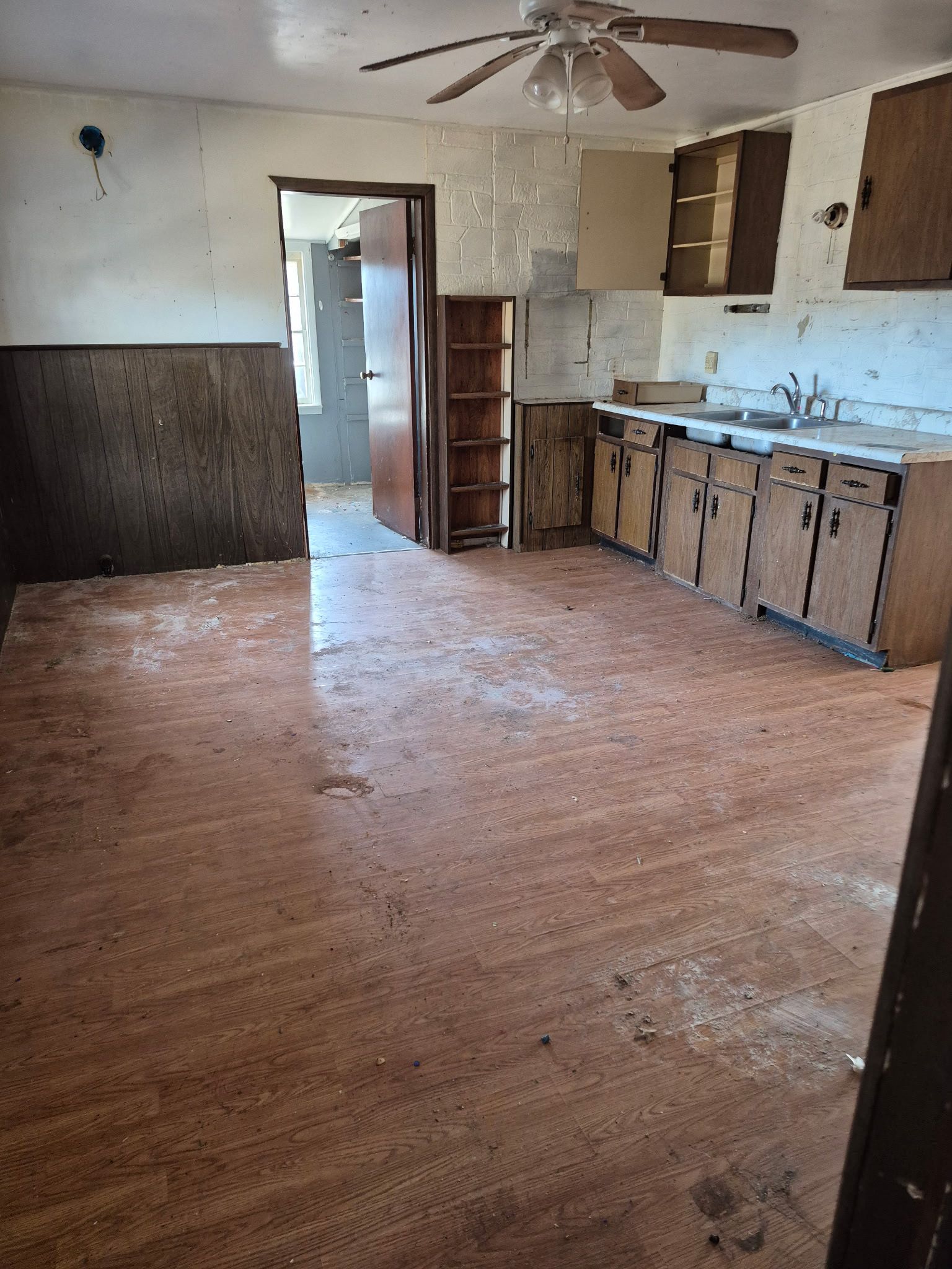 Dirt clearing with a tree, a brick, and a stick. Brown leaves and trees in the background under a blue sky.