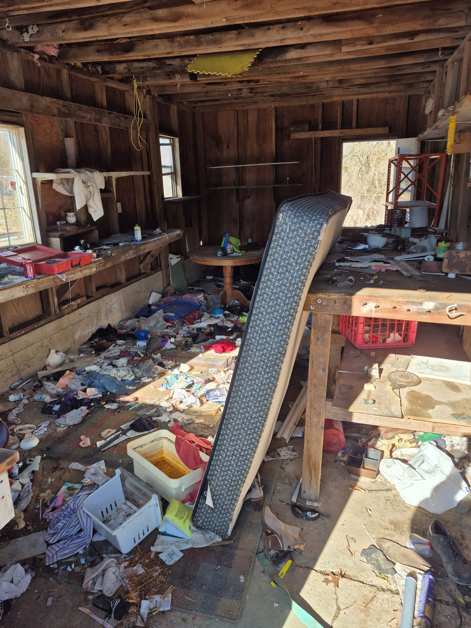 Messy interior of a dilapidated building with debris, exposed wood beams, and trash scattered throughout.