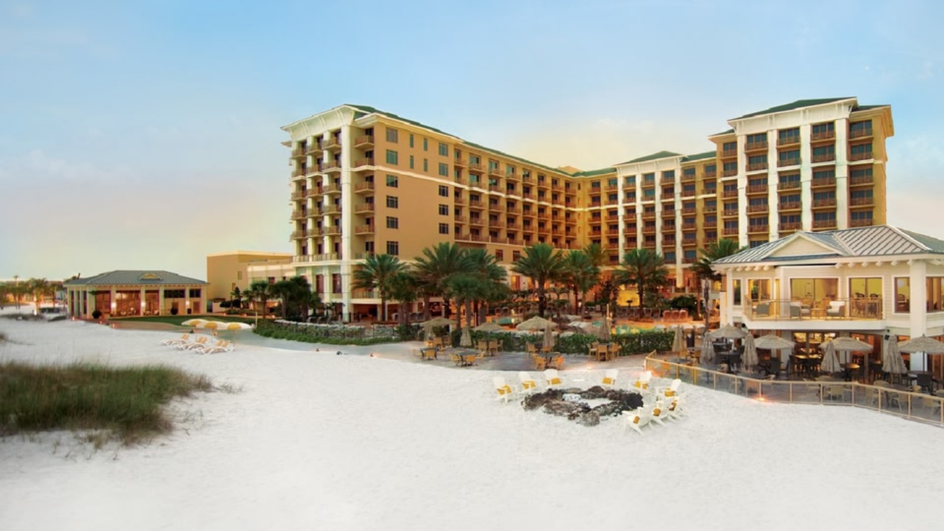 Beachfront resort with tall tan buildings, white sand, and outdoor dining at sunset