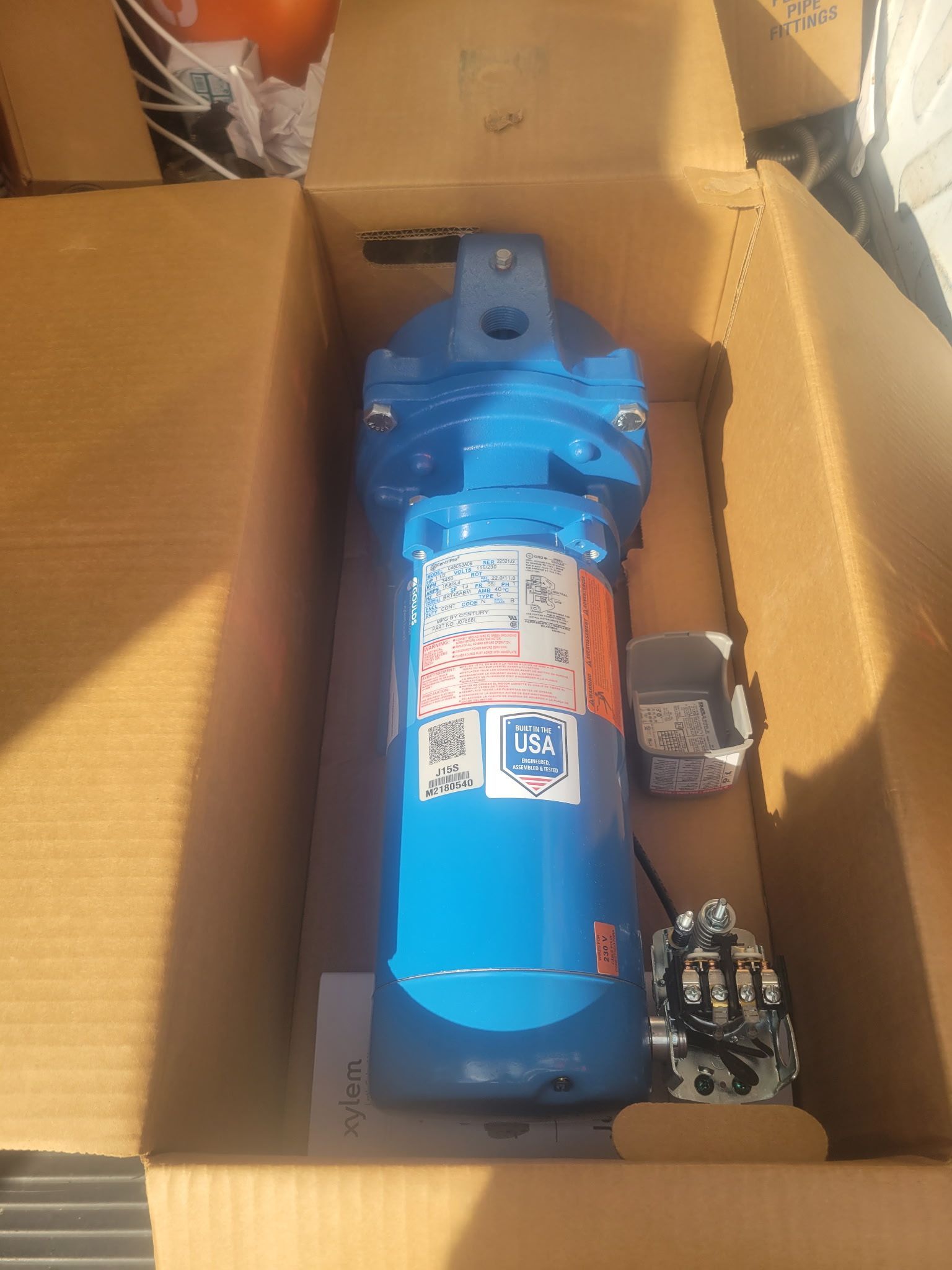 Blue industrial motor or pump in a cardboard box, surrounded by packing material.